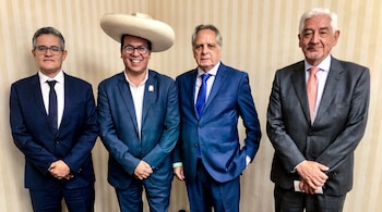 Cuatro hombres de pie, vestidos con traje. Uno de ellos, el segundo de la izquierda, lleva un sombrero de ala ancha. Fondo de pared con rayas claras.