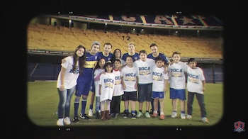 Niall Horan y Ellis Platten de pie junto a ocho niños en un campo de fútbol, con las gradas de un estadio de Boca Juniors al fondo