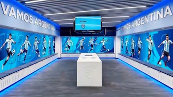 Sala interior con decoración azul y blanca, paneles que muestran imágenes de futbolistas de la selección argentina y el texto 'VAMOS ARGENTINA'. Un banco blanco central
