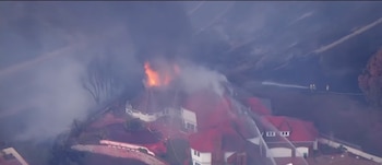 Vista aérea de una casa con el tejado en llamas, humo denso alrededor y chorros de agua dirigidos hacia la estructura