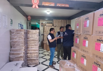 Tres trabajadores inspeccionan un almacén lleno de cajas de cartón apiladas con el logotipo de la ONPE y etiquetas rosadas