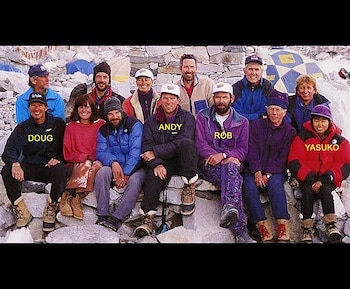 Once montañistas, incluyendo a Rob Hall, Doug Hansen y Yasuko Namba, posan sentados sobre rocas con ropa de invierno en un campamento de montaña