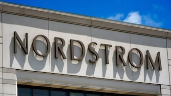 Primer plano del letrero "NORDSTROM" en letras oscuras tridimensionales sobre una fachada de edificio blanco, con cielo azul