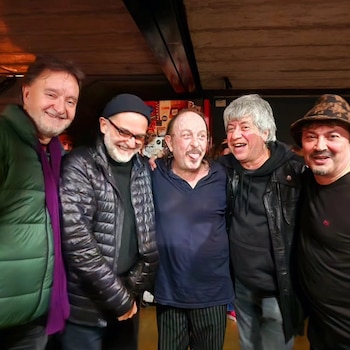 Cinco hombres sonríen e interactúan abrazados frente a la cámara en un espacio interior iluminado