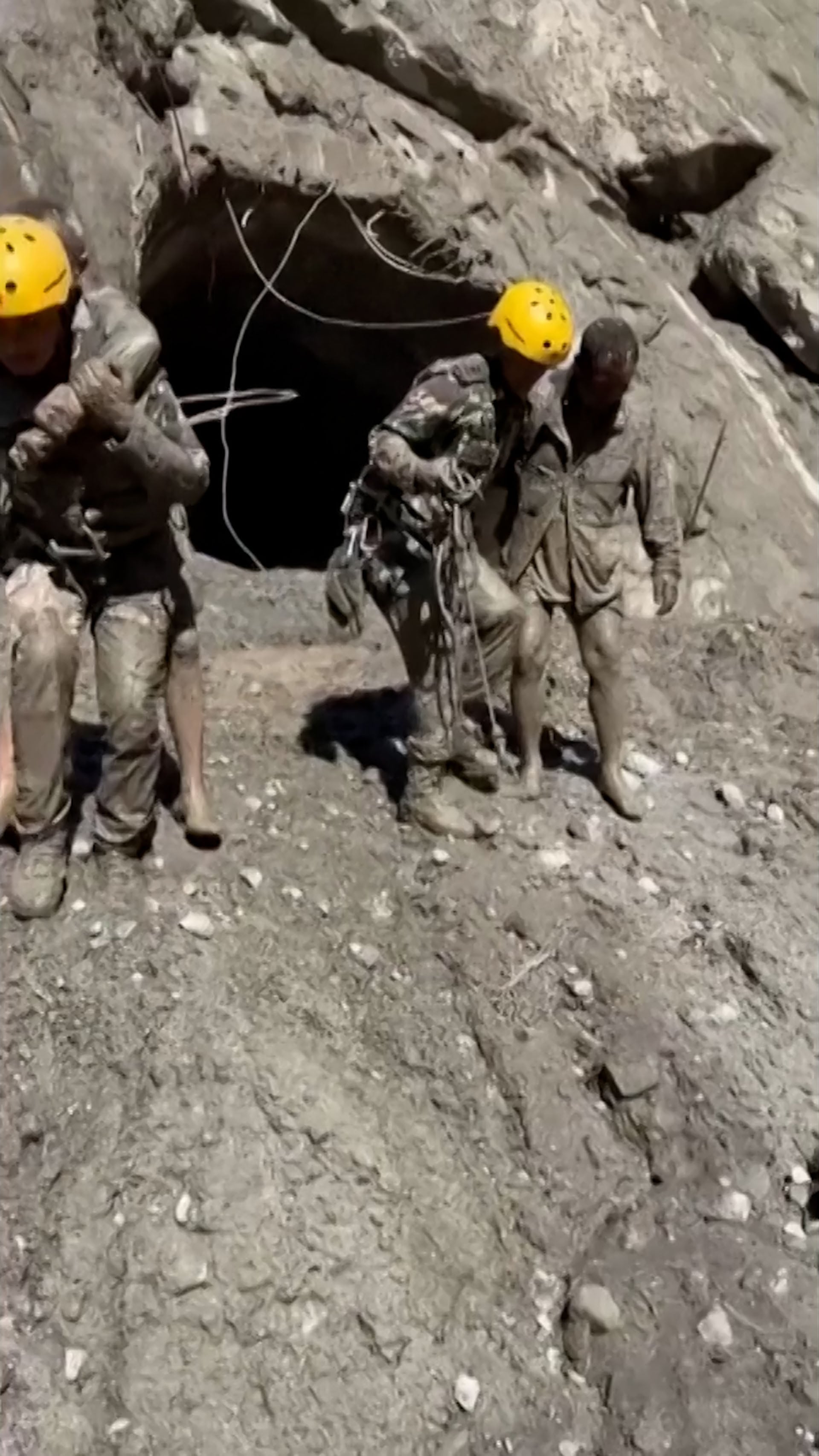 Varios rescatistas cubiertos de lodo auxilian a personas atrapadas cerca de una estructura rocosa en Nepal (Captura de video)