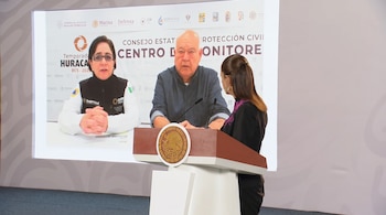 Una mujer parada junto a un podio con el escudo de Estados Unidos Mexicanos frente a una pantalla con dos personas en videollamada.
