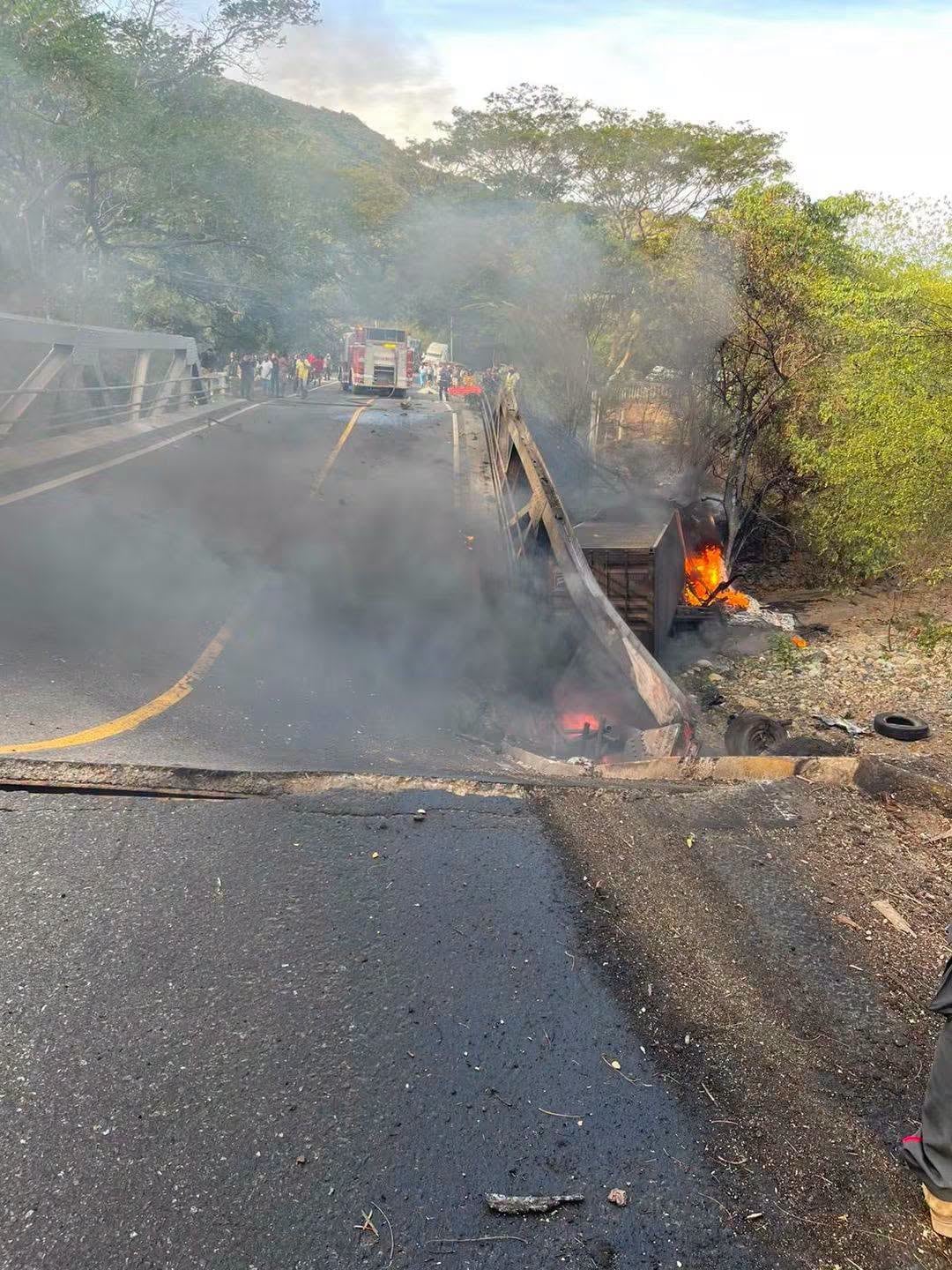 Un vehículo accidentado se incendia a un costado de un puente mientras efectivos de bomberos atienden la emergencia. (La noche informativa)