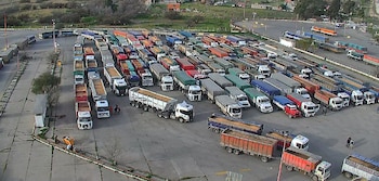 Vista aérea de decenas de camiones de carga con acoplado estacionados en filas sobre una playa pavimentada