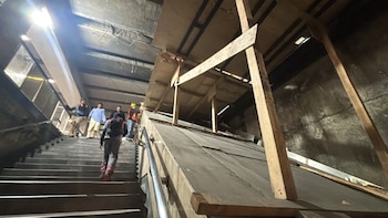 Personas suben escaleras en una estación oscura del Metro CDMX, con andamios de madera y cubiertas temporales de construcción a la derecha
