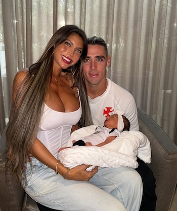 Cielo López y Claudio Spinelli están sentados frente a una cortina y sostienen a un bebé recién nacido envuelto en una manta blanca