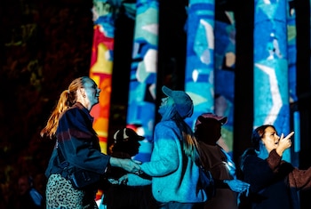 Varias personas reciben la luz de proyecciones azules y amarillas frente a columnas con patrones de colores durante la noche