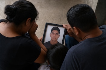 Tres personas vistas desde arriba y de espaldas sostienen el retrato enmarcado de un joven.