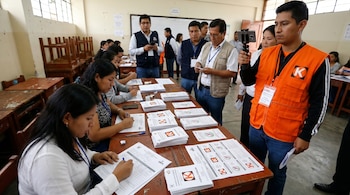 Miembros de mesa cuentan cédulas de votación en un aula escolar. Un personero de Fuerza Popular con chaleco naranja graba el proceso con un smartphone.