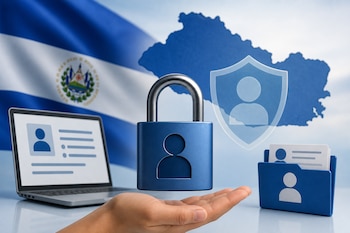 Una mano sostiene un candado azul con el diseño de un usuario frente a una computadora portátil, una carpeta y la bandera de El Salvador.