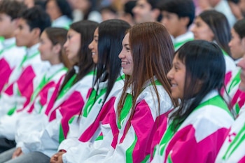 Un grupo de jóvenes sentados en filas viste chaquetas deportivas de color blanco, verde y rosa