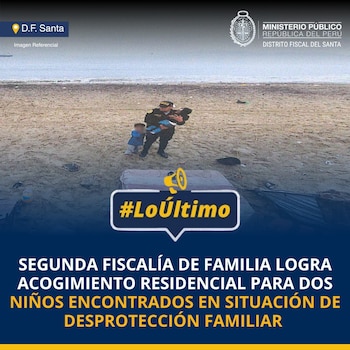 Un policía uniformado carga a un niño mientras otro menor lo observa en una playa de arena. Al fondo se ve el mar y objetos sobre la arena