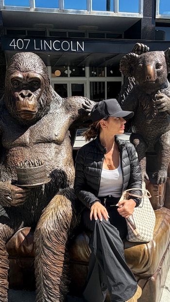 Mujer con gorra y chaqueta negra sentada entre dos estatuas de animales de bronce (gorila y koala) frente a un edificio con el letrero '407 LINCOLN'