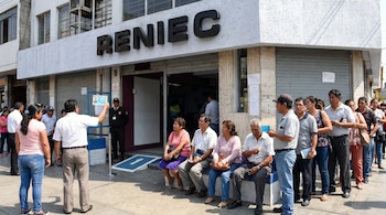 Vista exterior de una oficina de RENIEC con personas esperando en fila y sentadas en un banco. Un hombre sostiene un DNI azul. Se ve un guardia de seguridad.