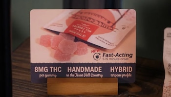 Cartel publicitario con varias gomitas rosadas, un empaque de producto y texto que detalla "8MG THC" y "Fast-Acting" en una base de madera