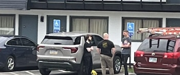 Tres hombres están de pie junto a varios automóviles estacionados frente a un edificio con señales de estacionamiento accesible