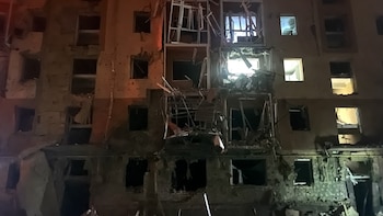 Fachada de un edificio residencial durante la noche con muros dañados, balcones destruidos, marcos desprendidos y ventanas rotas