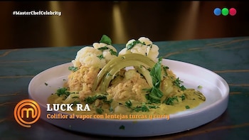 Un plato blanco con coliflor cocida, lentejas, salsa de curry amarillo y hierbas verdes picadas sobre una superficie oscura