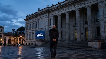 Un hombre de espaldas con toga ante un edificio de piedra con columnas y una pantalla iluminada con el texto Justicia y Constitución.