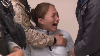Una mujer llora con la boca abierta mientras un agente con uniforme de camuflaje sostiene su hombro y pecho