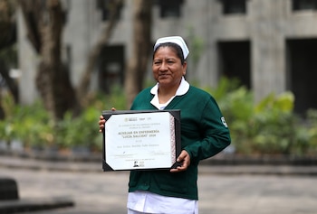 Vista lateral de varias personas sentadas en butacas rojas, aplaudiendo. En primer plano, dos mujeres con cofias de enfermera; una viste de blanco, otra de verde