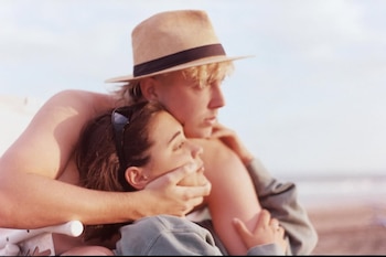Primer plano de dos personas abrazándose. Una de ellas usa un sombrero color beige y la otra lleva gafas de sol sobre el cabello