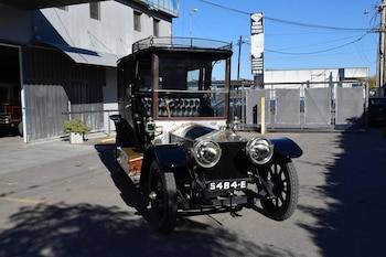 Un automóvil antiguo de color negro y plateado con faros circulares grandes y matrícula 5484-E estacionado frente a un edificio