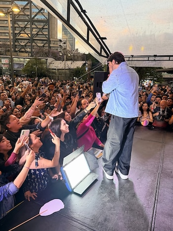 Luis Fonsi de espaldas en el escenario, vistiendo chaqueta de mezclilla, frente a una multitud de fans que levantan sus teléfonos para grabar