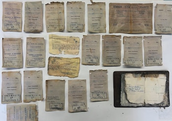 Fila de recibos de papel antiguo impresos en alemán junto a una libreta abierta con anotaciones hechas a mano sobre un fondo blanco