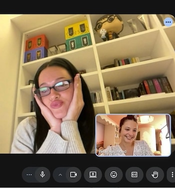 Pantalla de videollamada con una mujer de gafas haciendo un gesto divertido en el recuadro principal, con estantería y libros detrás