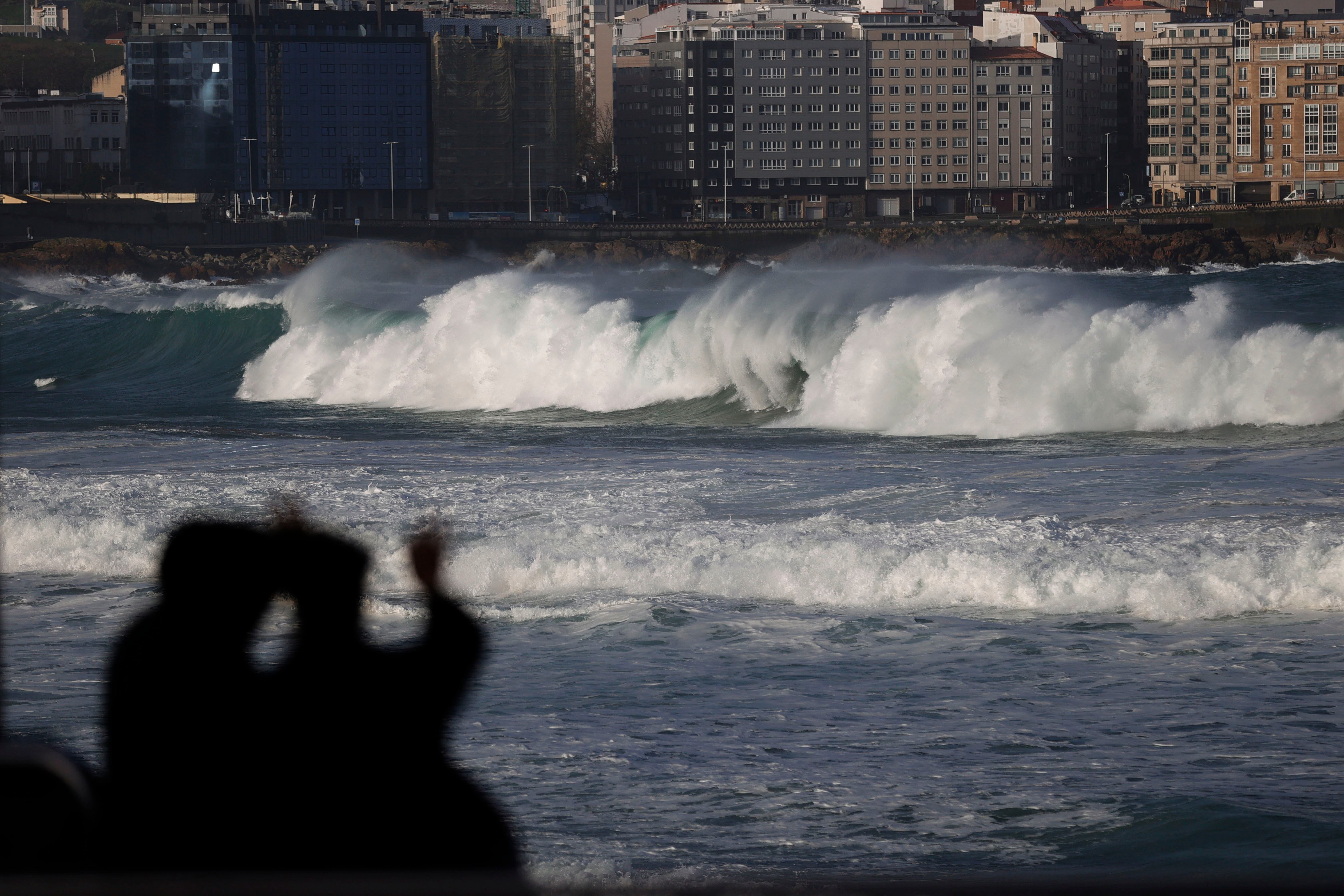 Dos personas observaban este viernes la ensenada del Orzán de A Coruña, donde la Aemet mantiene activo el nivel de alerta roja en el mar, con mar combinado que podría dejar olas de 8 metros. (Cabalar/EFE)