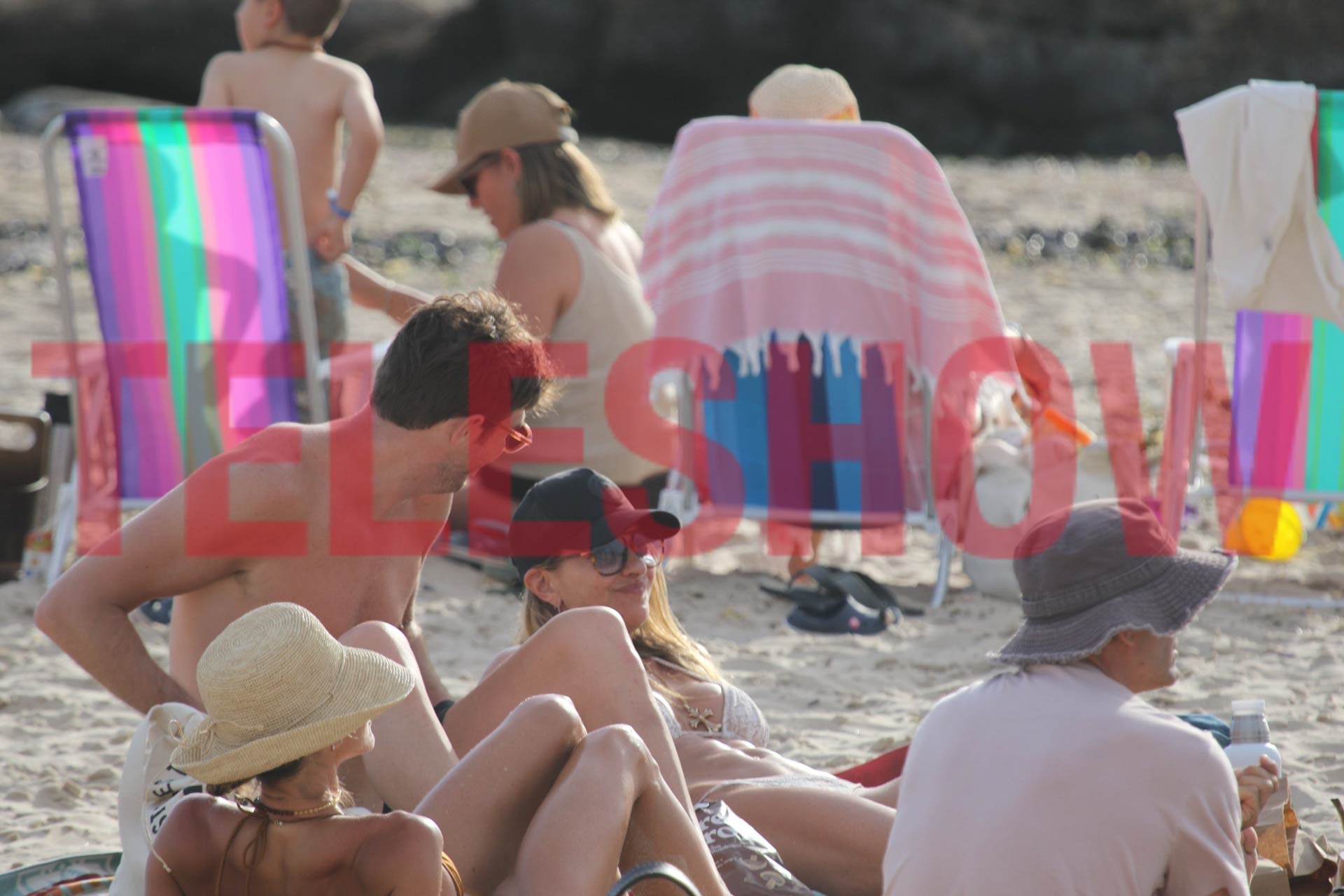 La modelo lució bikini clara y gafas de sol mientras se relajaba en la arena, conversando y sonriendo en compañía