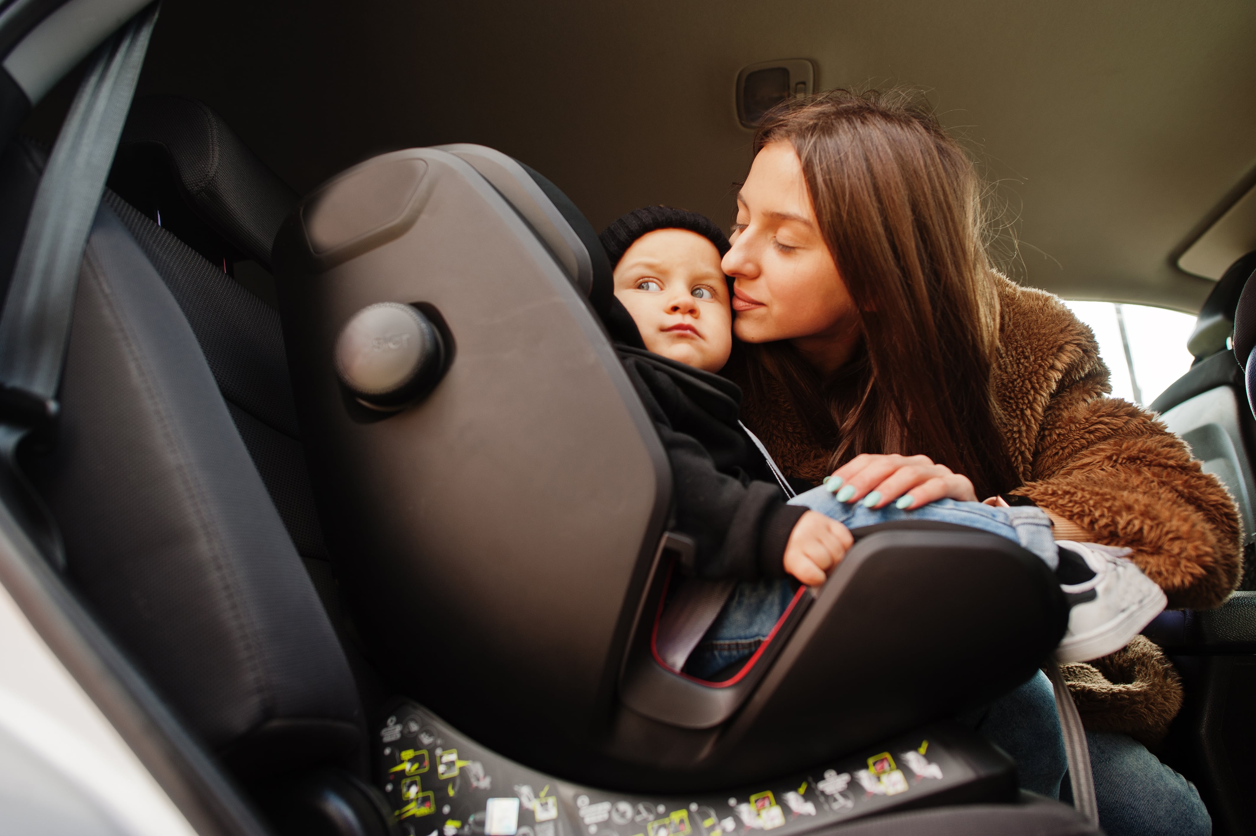 Una madre montando a su hijo en la silla del coche (Freepik)