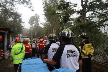 Cuatro bomberos con cascos y chaquetas amarillas y rojas asisten a una persona cerca de una lona blanca en una pendiente