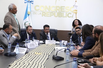 Diputados y funcionarios reunidos en una mesa de conferencia frente a un muro con las letras Congreso de la República y la bandera de Guatemala