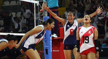 Tres jugadoras de voleibol de la selección de Perú celebran en una cancha con una red y público en las gradas