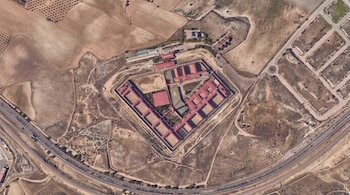 Vista aérea de un complejo penitenciario con tejados rojos, muros de seguridad, campos agrícolas y carreteras a su alrededor.