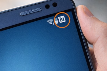 Primer plano de un smartphone con un círculo naranja rodeando el icono de NFC (letra N) en la parte superior derecha de la pantalla azul.