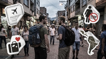 Dos hombres con mochilas caminan en una calle concurrida, rodeados de stickers que incluyen un avión "Passport", una maleta con corazón, "Stop Exploitation" y un mapa de Latinoamérica.