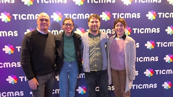 Cuatro personas, dos hombres y dos mujeres, de pie y sonrientes, frente a una pared de fondo morado con el logo de Ticmas