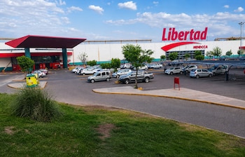 Estacionamiento con automóviles frente a un gran edificio blanco con el cartel rojo de Libertad Mendoza y césped en primer plano