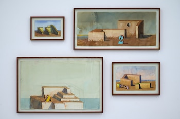 Cuatro acuarelas enmarcadas de Fernando Maza, con edificios geométricos, paisajes marinos y números, cuelgan en una pared blanca