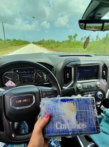 Una mano sostiene un paquete envuelto en plástico con la leyenda Con Dios desde el interior de un vehículo en una carretera