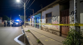 Vivienda modesta de noche en Juchitán de Zaragoza acordonada con cinta amarilla 'prohibido el paso'. Patrulla policial y personal forense al fondo desenfocado.