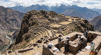 Vista aérea de arqueólogos trabajando en las ruinas de piedra de la ciudadela inca de T'aqrachullo, rodeada de montañas escarpadas y un río sinuoso