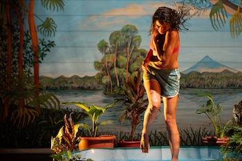 Dos personas, un hombre y una mujer, se relajan en colchonetas en un escenario oscuro con un telón de fondo tropical y elementos como frutas y plantas